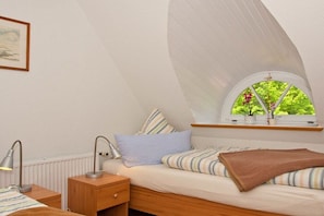 A bedroom with a sloped ceiling, a window with a view of greenery, a bedside table with a lamp, and a bed with striped bedding. - Thatched roof house - House 2 (Wittdün auf Amrum)
