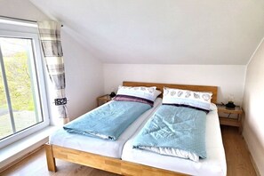 A bedroom with two beds, a window with curtains, and a nightstand with a lamp. - Holiday apartment with 2 bedrooms (Pellworm)