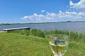 Un bicchiere di vino bianco sull'erba, vicino a un corso d'acqua con un pontile e un'isola in lontananza.