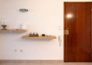 Een kamer met een houten deur, twee wandplanken met verschillende voorwerpen, een wandlamp en een telefoon.