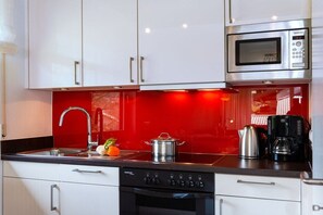 Una cocina moderna con gabinetes blancos, un microondas de acero inoxidable y un salpicadero rojo.