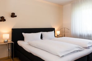 A hotel room with a large bed, two bedside tables, and a nightstand with a lamp. - Holiday apartment with 1 bedroom (Garmisch-Partenkirchen)