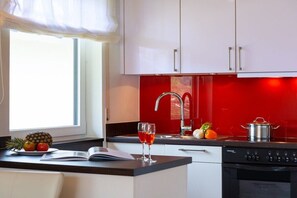 A modern kitchen with white cabinets, a red backsplash, a stainless steel sink, and a black stove. - Holiday apartment with 1 bedroom (Garmisch-Partenkirchen)