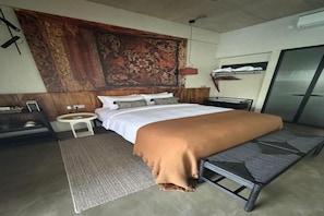 Un dormitorio con una cama grande, una mesita de noche, un taburete pequeño, un banco y un tapiz en la pared.