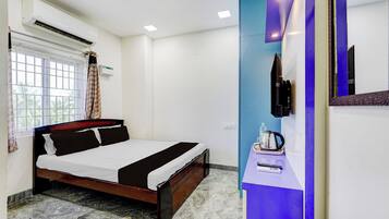 Une chambre d’hôtel comprenant un lit, une fenêtre avec des rideaux, un appareil de climatisation, un téléviseur à écran plat fixé au mur, ainsi qu’une petite table avec une bouilloire et des télécommandes.