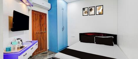 A bedroom with a bed, a wardrobe, a desk with a chair, a television, and a ceiling fan.