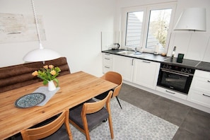 A modern kitchen with white cabinets, a wooden dining table, and a built-in oven. - Cloud (Holiday home Haldern) (Rees)