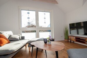 A living room with a sofa, a coffee table, a TV, and a large window with decorative elements. - Cloud (Holiday home Haldern) (Rees)