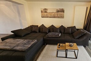 A modern living room with a sectional sofa, a small wooden coffee table, and a painting on the wall. - Holiday apartment on the edge of the forest (Wassenberg)