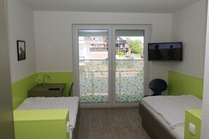 Una habitación con dos camas, televisor, escritorio y ventana con vista a edificios.