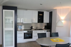 Eine moderne Küche mit weißen Schränken, einem eingebauten Backofen und einem Essbereich mit rundem Tisch und Stühlen.