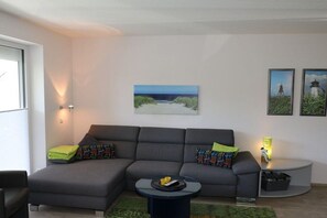 Ein modernes Wohnzimmer mit einem grauen Modulsofa, einem kleinen runden Couchtisch und einem Bild von einer Strandansicht an der Wand.