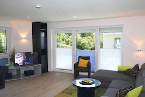 Ein modernes Wohnzimmer mit Flachbildfernseher, einer Couch, einem Couchtisch und einem Sessel.