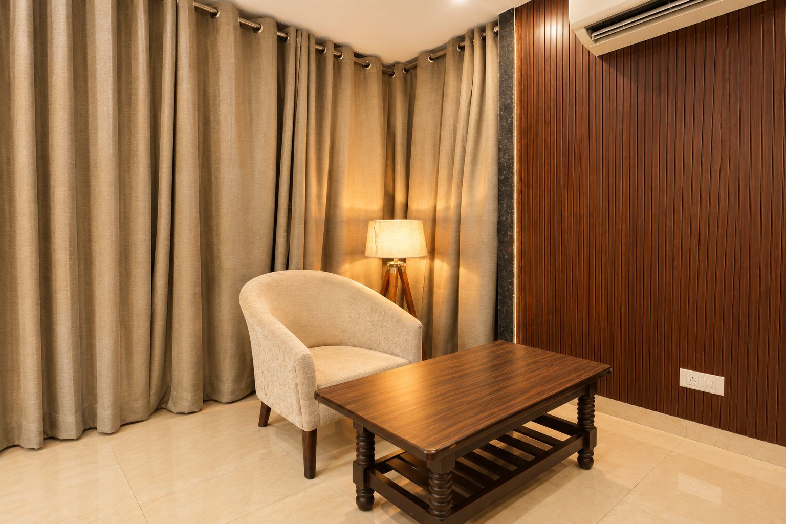 A room with a wooden table, a beige armchair, and a lamp.
