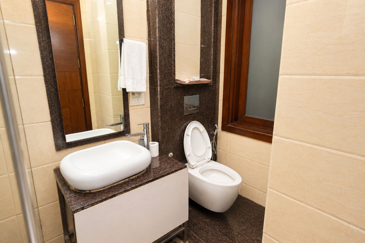 A bathroom with a white sink, a toilet, a mirror, and a towel hanging on the wall.