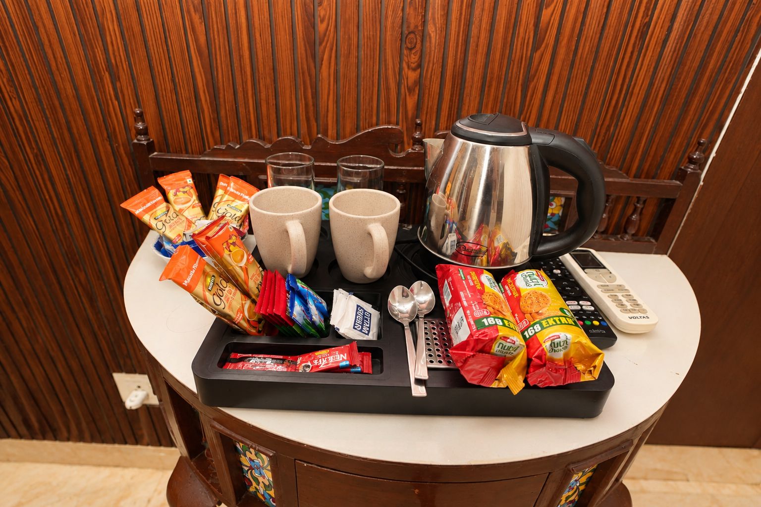 A tray with snacks, two mugs, a kettle, and a remote control on a table.