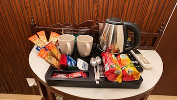 A tray with snacks, two mugs, a kettle, and a remote control on a table.