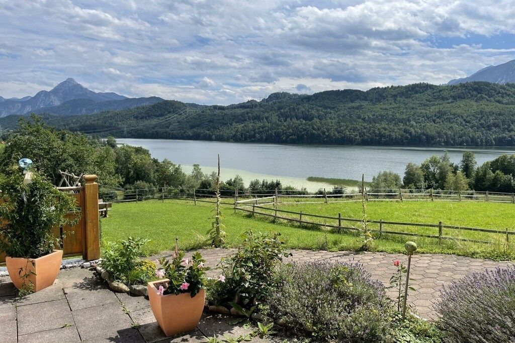 A view of a lake with mountains in the background, a wooden fence, and potted plants in the foreground.