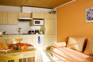 A compact kitchen with wooden cabinets, a microwave, and a dining area with a table set for a meal. - 3 - at the Füssen equestrian center (Weißensee-Füssen)