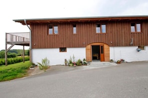 A two-story wooden building with a balcony on the upper level, a wooden door, and a small porch area with potted plants. - Holiday apartment with 2 bedrooms (Scheggerott)