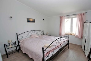A bedroom with a metal bed frame, a bedside table with a lamp, a window with curtains, and a wall-mounted picture. - Holiday apartment with 2 bedrooms (Scheggerott)