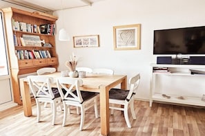 Un coin repas avec une table et des chaises en bois, une bibliothèque, un téléviseur à écran plat et des tableaux encadrés accrochés au mur.