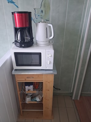 A compact kitchen setup with a microwave, a coffee maker, and a kettle on a small wooden cabinet.