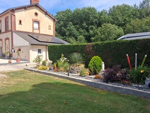 A building with a sloped roof and a garden with various plants and a statue.