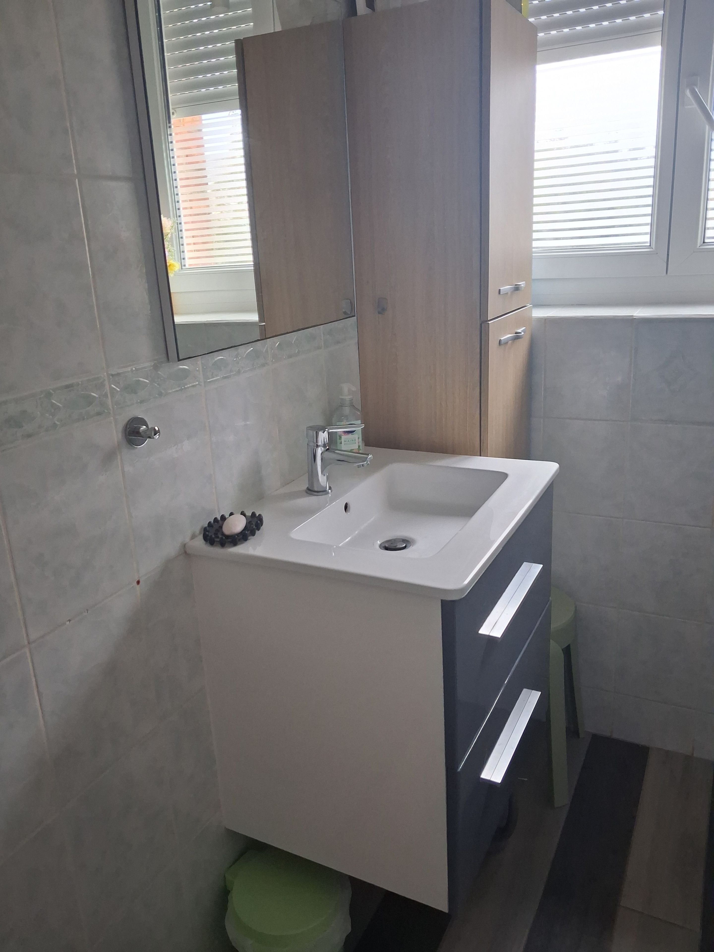Un baño con un lavabo blanco, un espejo encima y un mueble de madera debajo.
