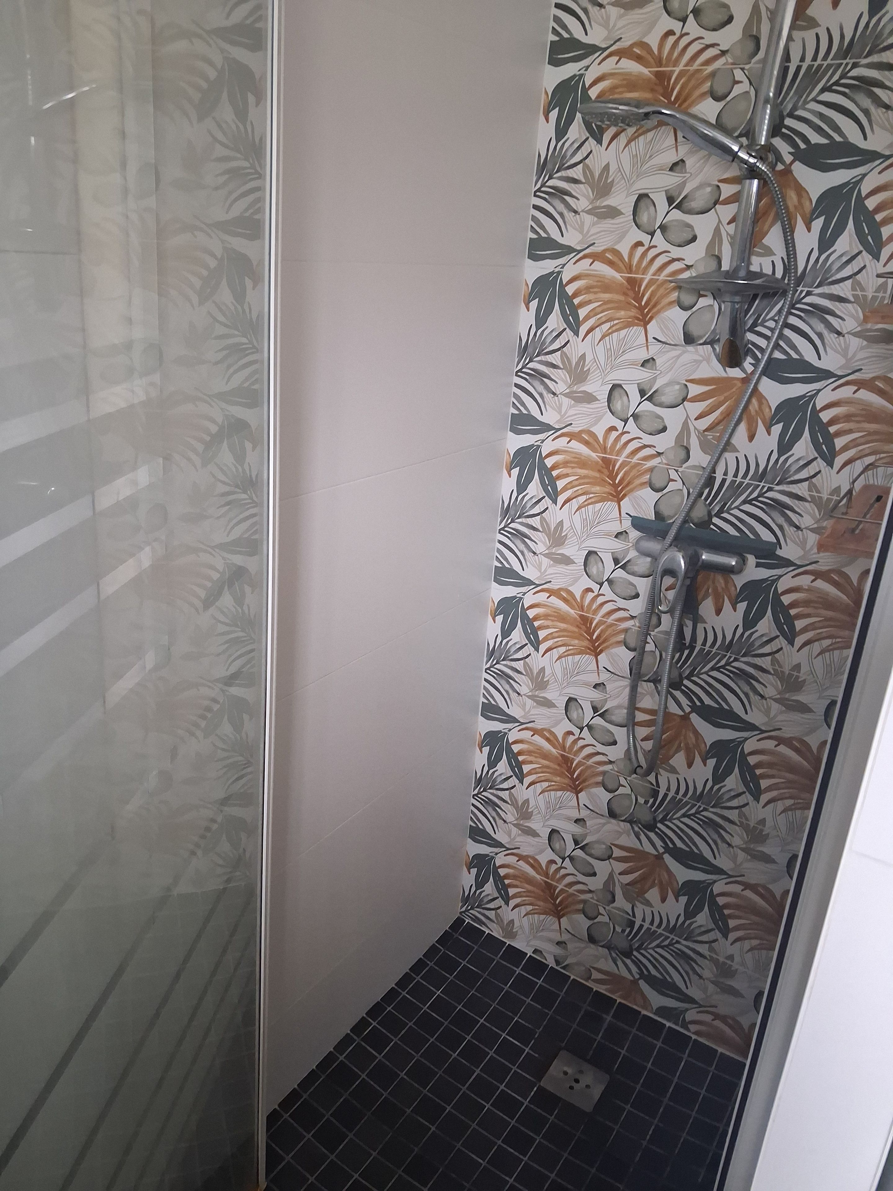Une douche avec des carreaux muraux à motifs floraux, une porte en verre et un sol carrelé.