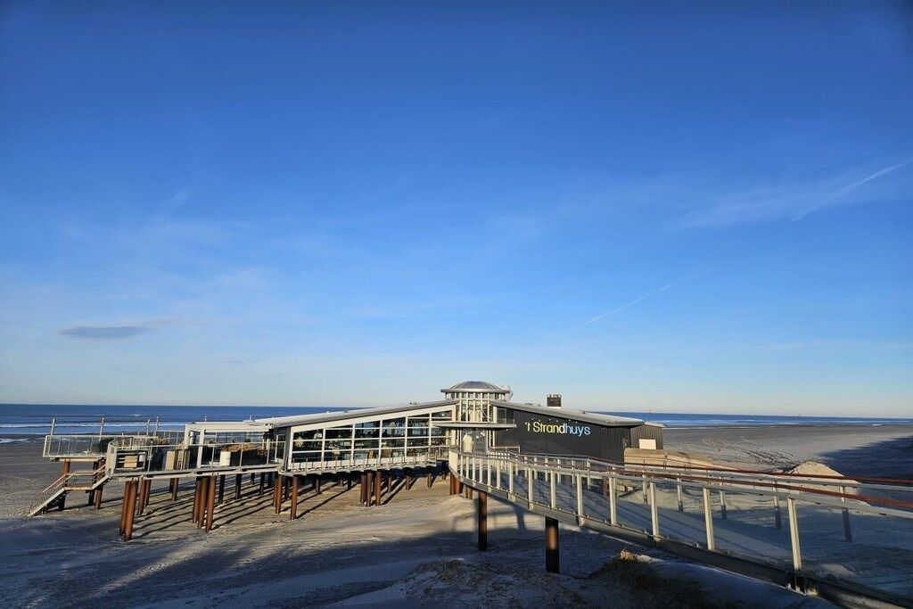 Ein Steg am Strand mit einer Aussichtsplattform und einem Gebäude mit der Aufschrift 'Strandhuyis'.
