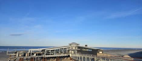 Ein Steg am Strand mit einer Aussichtsplattform und einem Gebäude mit der Aufschrift 'Strandhuyis'.