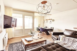 A modern living room with a flat-screen TV, a wooden coffee table, a brown leather sofa, and a dining area with a table and chairs. - Holiday apartment with 1 bedroom (Buren\/Ameland)
