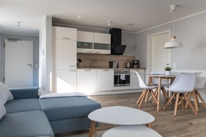 A modern kitchen with white cabinets, a black range hood, and a dining area with white chairs and a round table. - Holiday apartment in Büsum with swimming pool (Büsum)