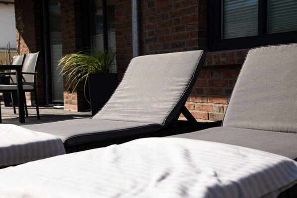 A sunlit outdoor seating area with lounge chairs and a potted plant. - Holiday apartment in Büsum with swimming pool (Büsum)