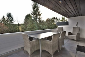 An outdoor patio with a table and chairs, a TV mounted on the wall, and a view of trees and hills. - Holiday apartment with 1 bedroom (Braunlage)