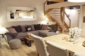 En moderne stue med en trætrappe, en grå sofa, et træsofabord og et spisebord med stearinlys.
