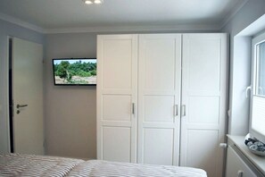 A bedroom with a bed, a wardrobe, a television mounted on the wall, and a window. - Holiday apartment with 1 bedroom (Braunlage)