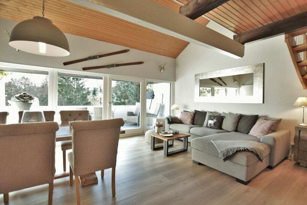 Un vaste espace de vie comprenant un canapé, une table à manger et des chaises, de grandes fenêtres et un plafond en bois.
