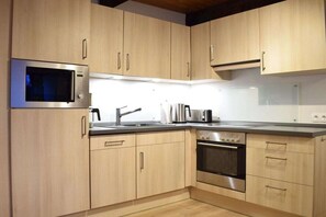 A modern kitchen with light wood cabinets, stainless steel appliances including a microwave, kettle, and oven, and a black faucet. - Holiday apartment with 1 bedroom (Braunlage)