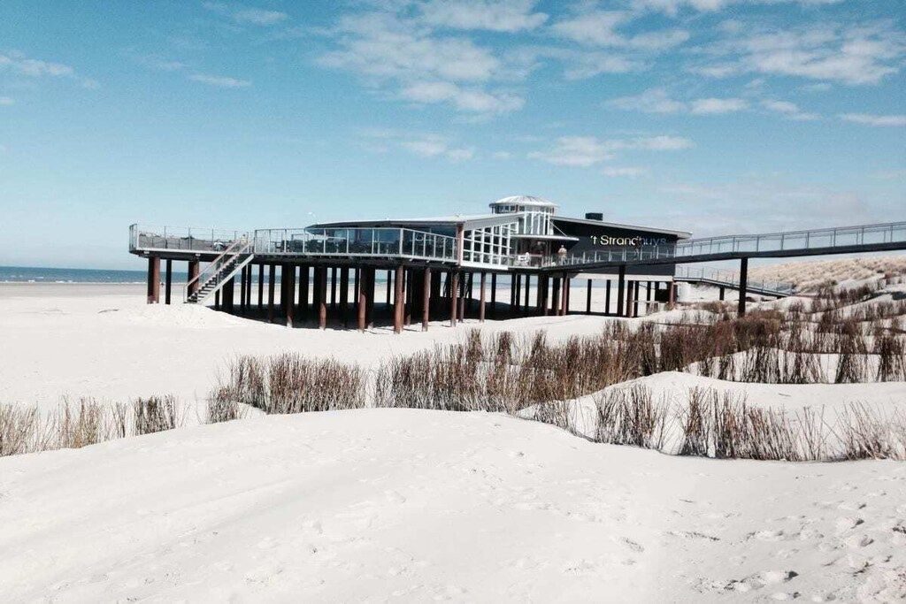 Ein Gebäude am Strand mit Glasfassade, einem überdachten Gang und einem Steg, der ins Wasser führt.