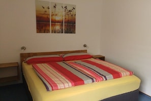 A bed with a striped bedspread and pillows, a wooden headboard, and a nightstand on each side. - 2 in the periwinkle house (Cuxhaven-Duhnen)