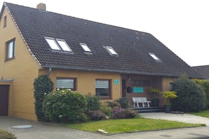 A two-story house with a sloped roof, a front porch with a bench, and a number '14' sign. - 2 in the periwinkle house (Cuxhaven-Duhnen)