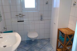 A bathroom with a white sink, toilet, and a wooden shelf with towels. - 2 in the periwinkle house (Cuxhaven-Duhnen)
