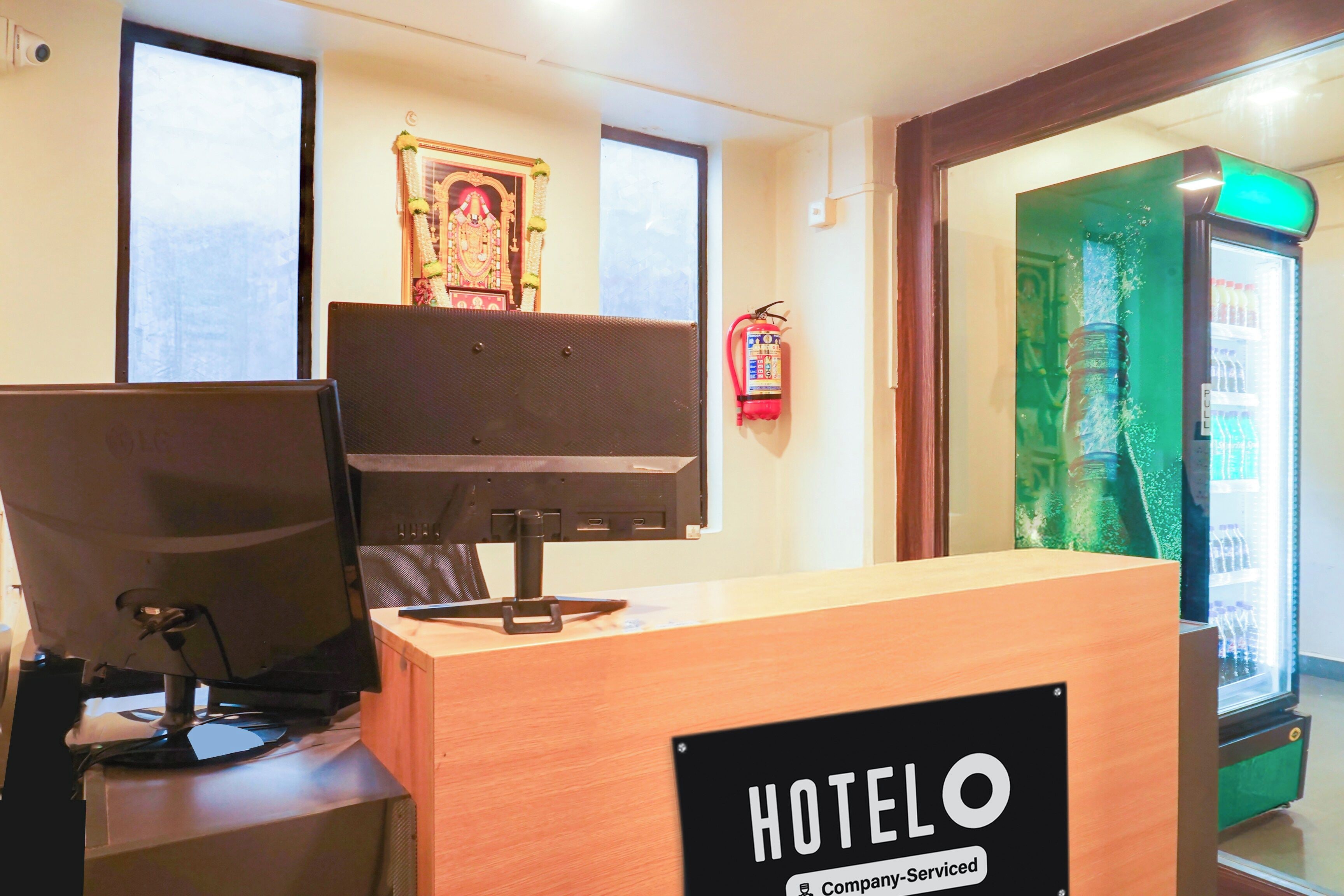 Una recepción de hotel con una computadora, un extintor y un refrigerador.