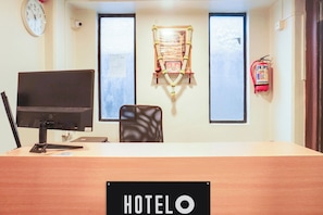 Mostrador de recepción de hotel con un monitor de computadora, una silla, un letrero que dice 'HOTEL O' y un extintor en la pared.