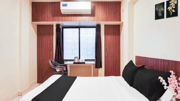 Habitación de hotel con cama, escritorio, silla, aire acondicionado y ventana con cortinas.