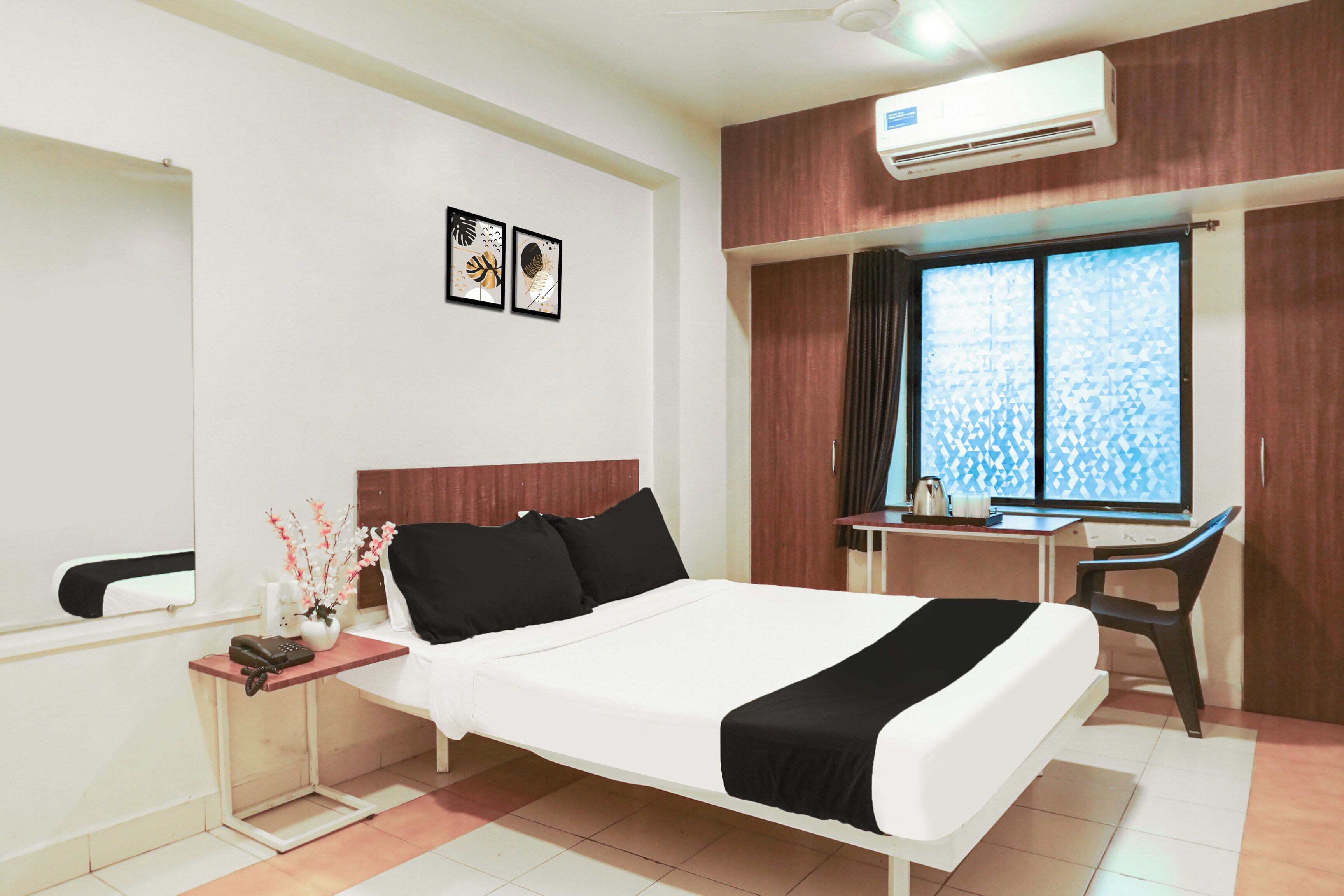A hotel room with a bed, a desk, a chair, a telephone, and a window with patterned curtains.