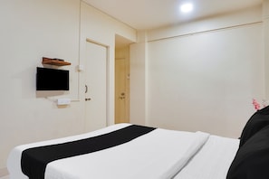 Habitación de hotel con una cama, un televisor montado en la pared y una puerta que da a otra habitación.