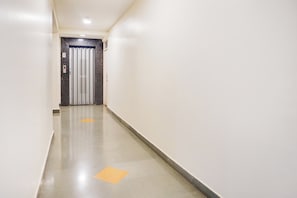 Un pasillo limpio y bien iluminado con una puerta al final, una barandilla y un suelo con indicaciones.
